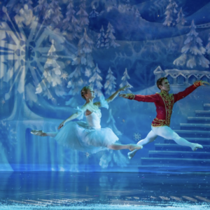 Two dancers perform gracefully on ice, surrounded by a winter wonderland backdrop of frosty trees and cascading water.
